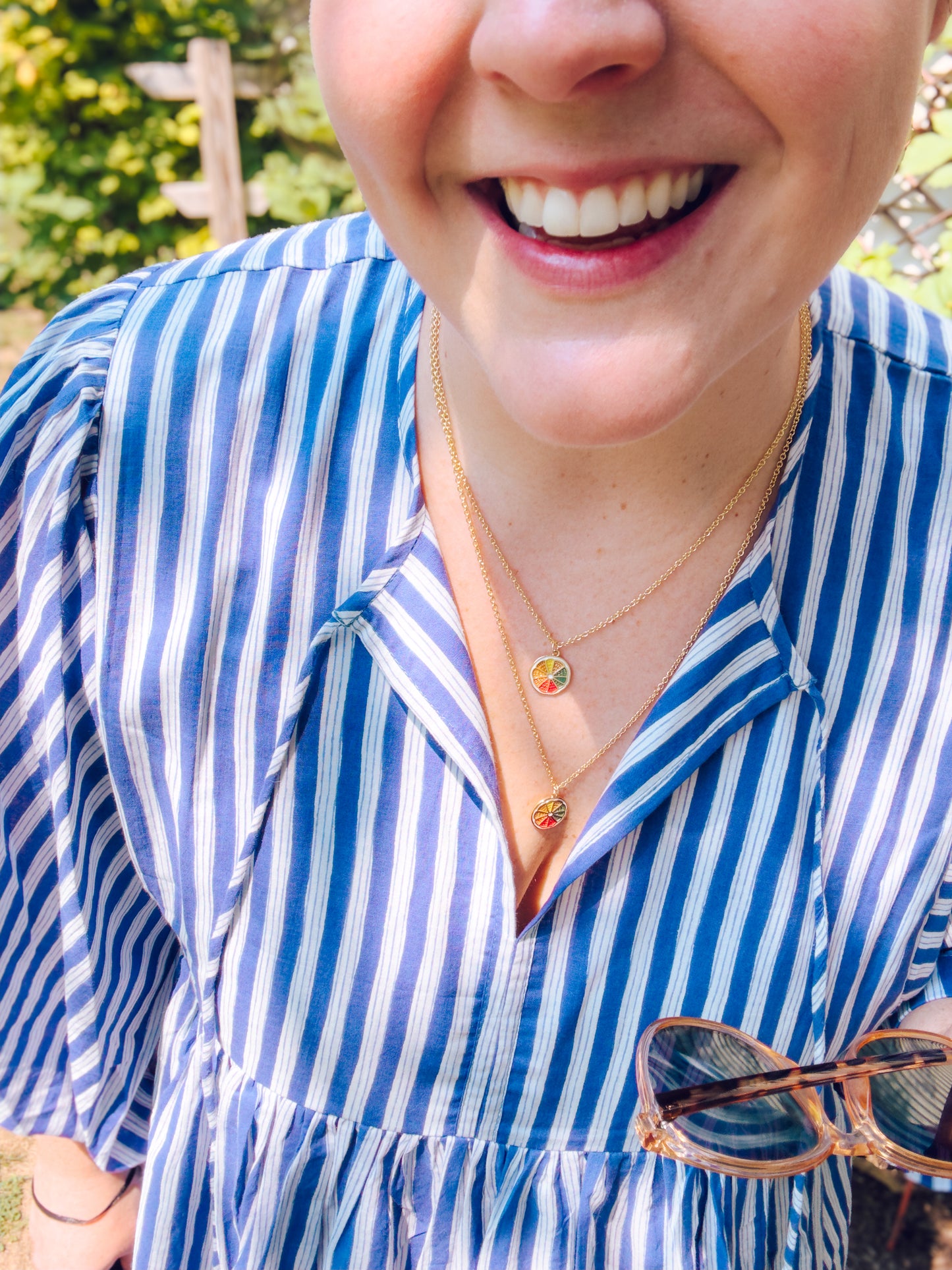 Person wearing a blue and white striped shirt with a necklace, outdoors.