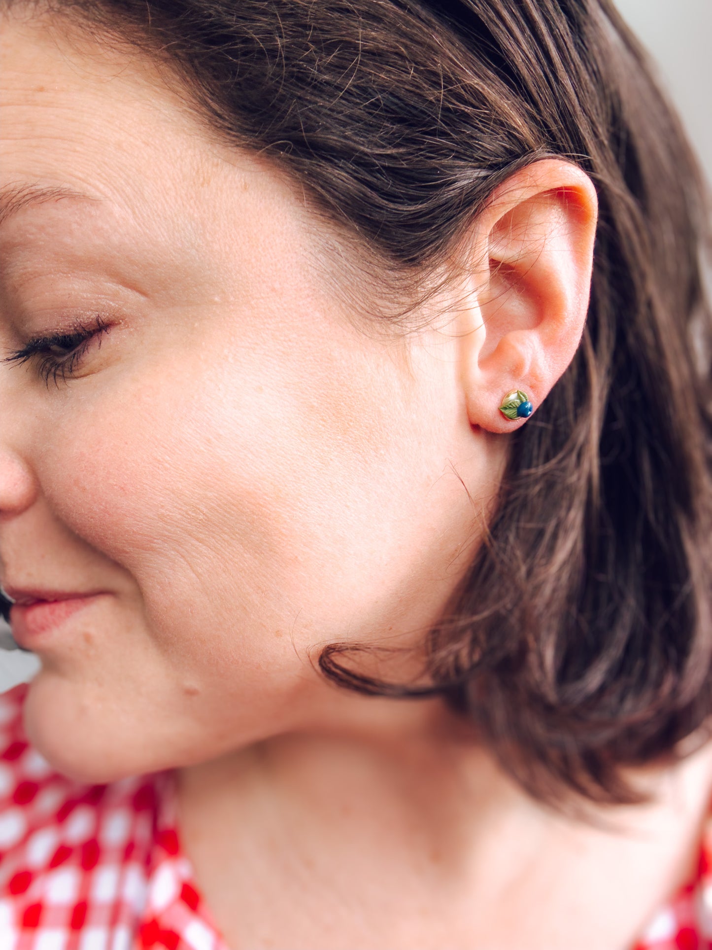 Close-up of a woman wearing a small earring with a red and white checkered shirt visible.