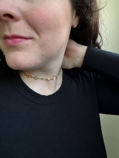 Person wearing a black shirt with a necklace featuring sunflower pendants.