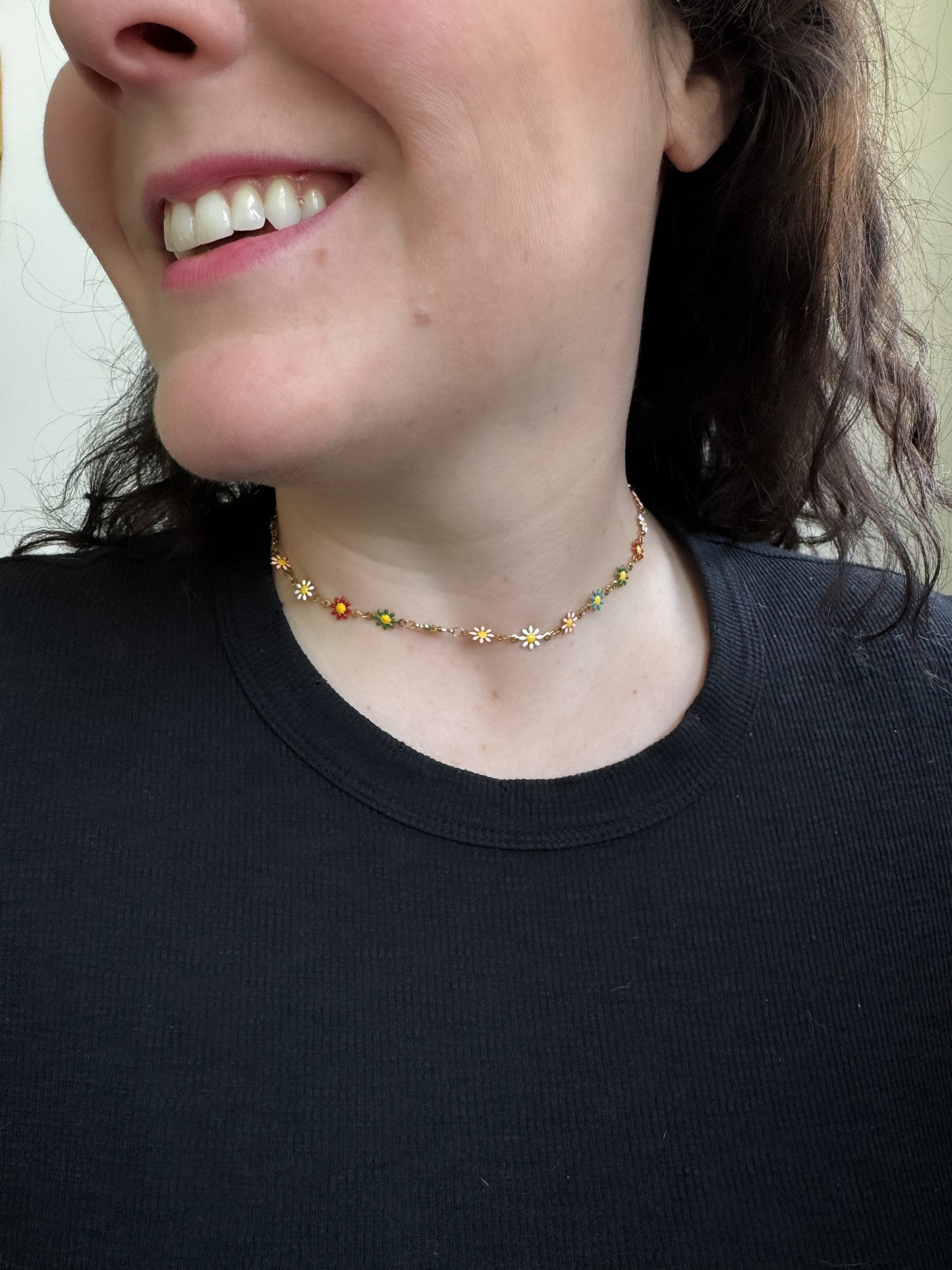 Person wearing a delicate necklace with small beads and flowers, smiling.