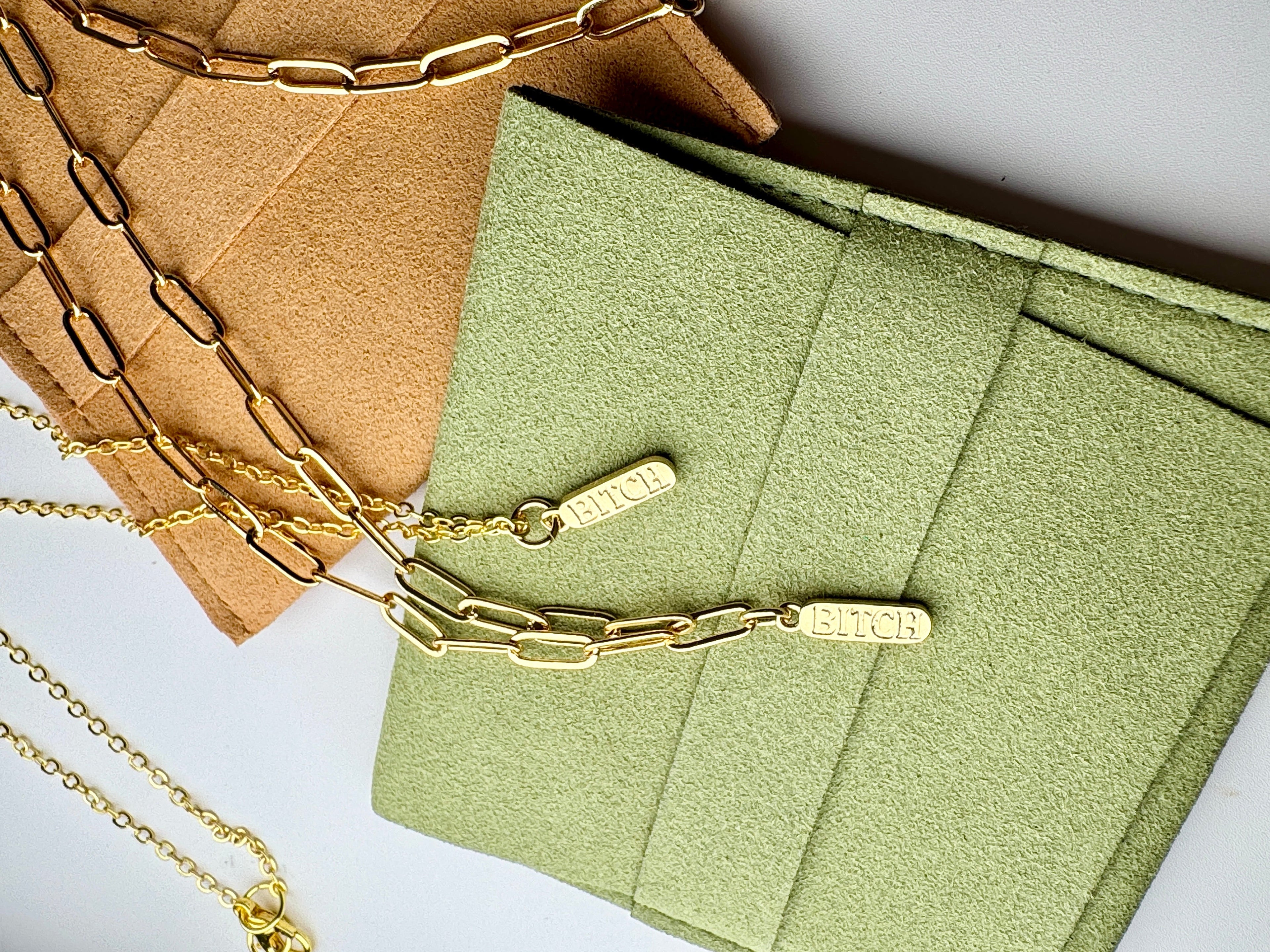 Gold chain necklaces on a green textured surface with a brown card in the background.