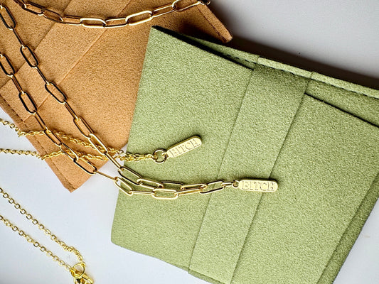 Gold chain necklaces on a green textured surface with a brown card in the background.
