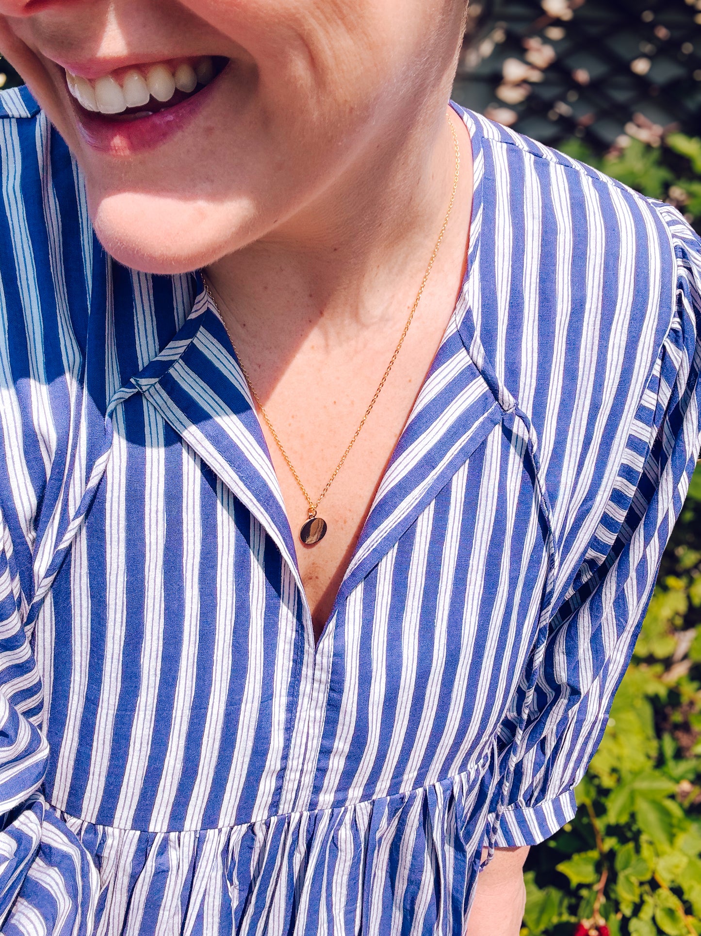 Person wearing a blue and white striped dress with a necklace, standing outdoors.