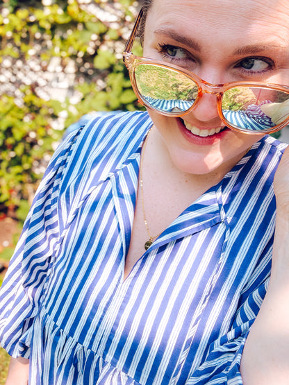 Person wearing a blue and white striped shirt with reflective sunglasses outdoors.