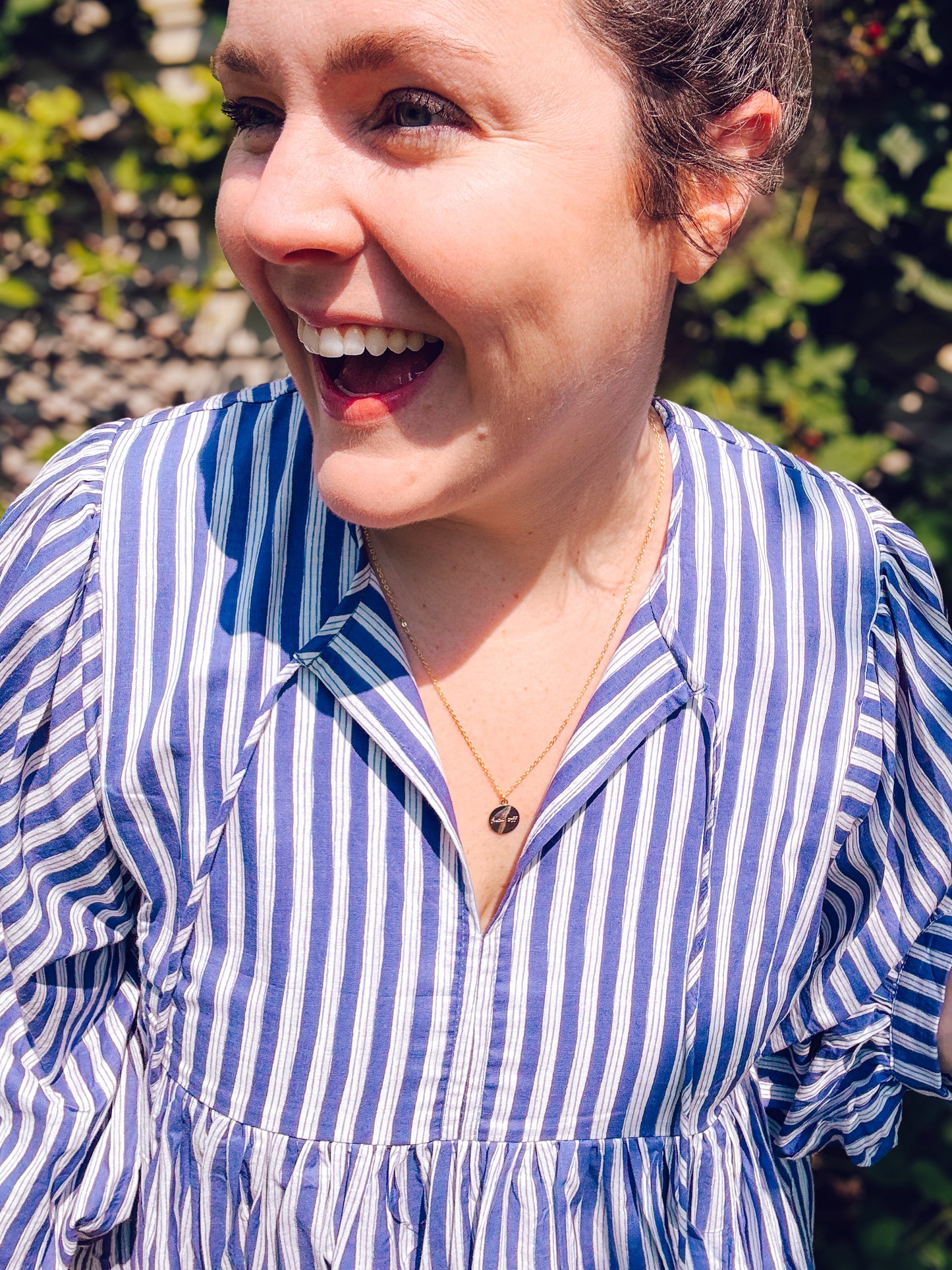 Woman wearing a blue and white striped shirt with a blurred green background