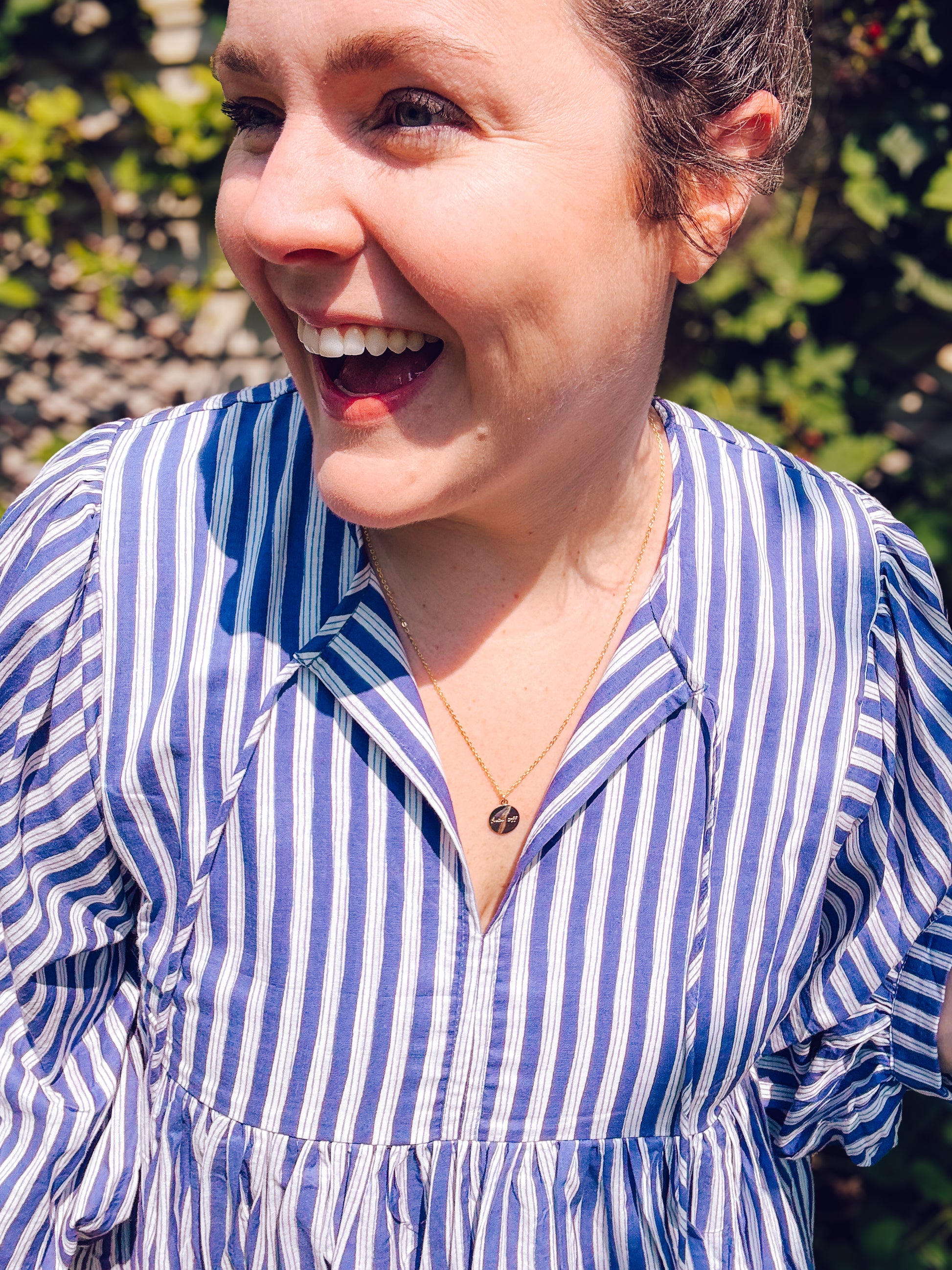Woman wearing a blue and white striped shirt with a blurred green background