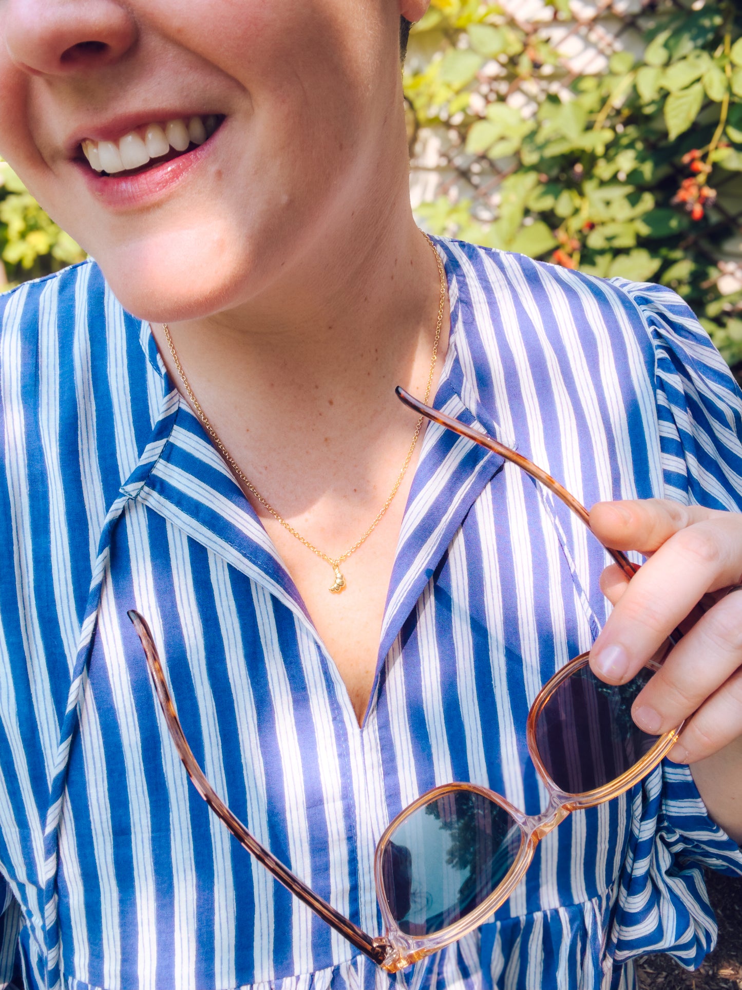 Person wearing a blue and white striped shirt holding sunglasses outdoors.