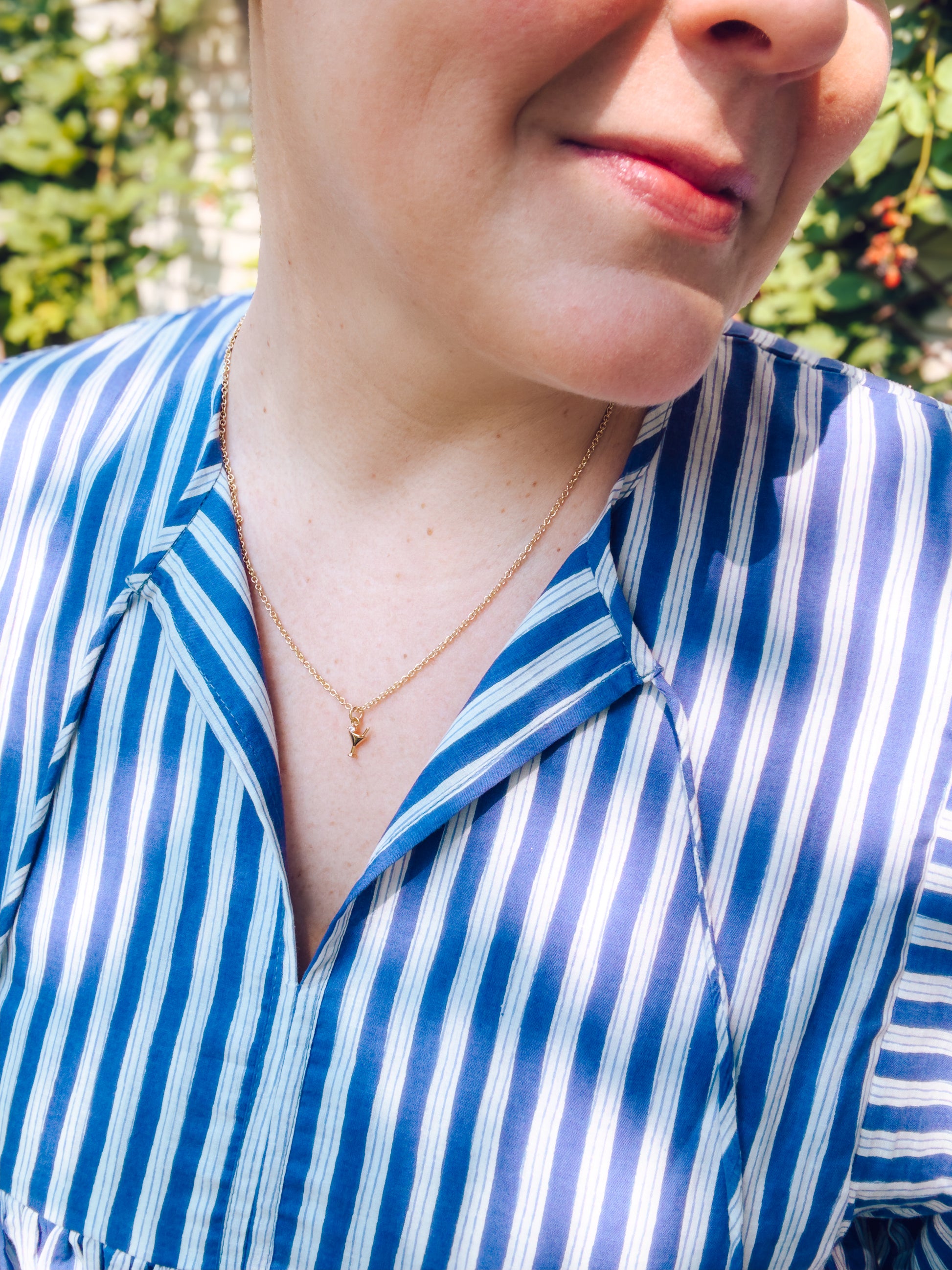 Person wearing a blue and white striped shirt with a necklace, outdoors.
