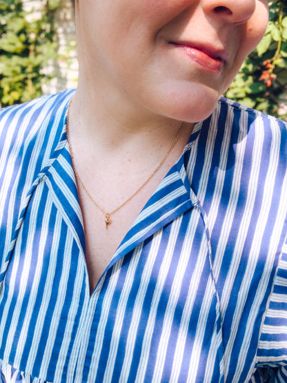 Person wearing a blue and white striped shirt with a necklace, outdoors.