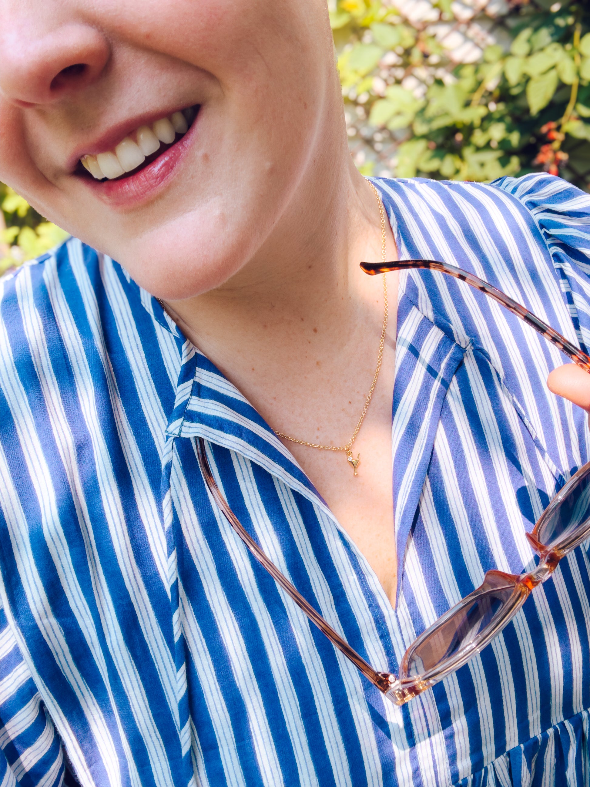 Person wearing a blue and white striped shirt with sunglasses on a blurred natural background