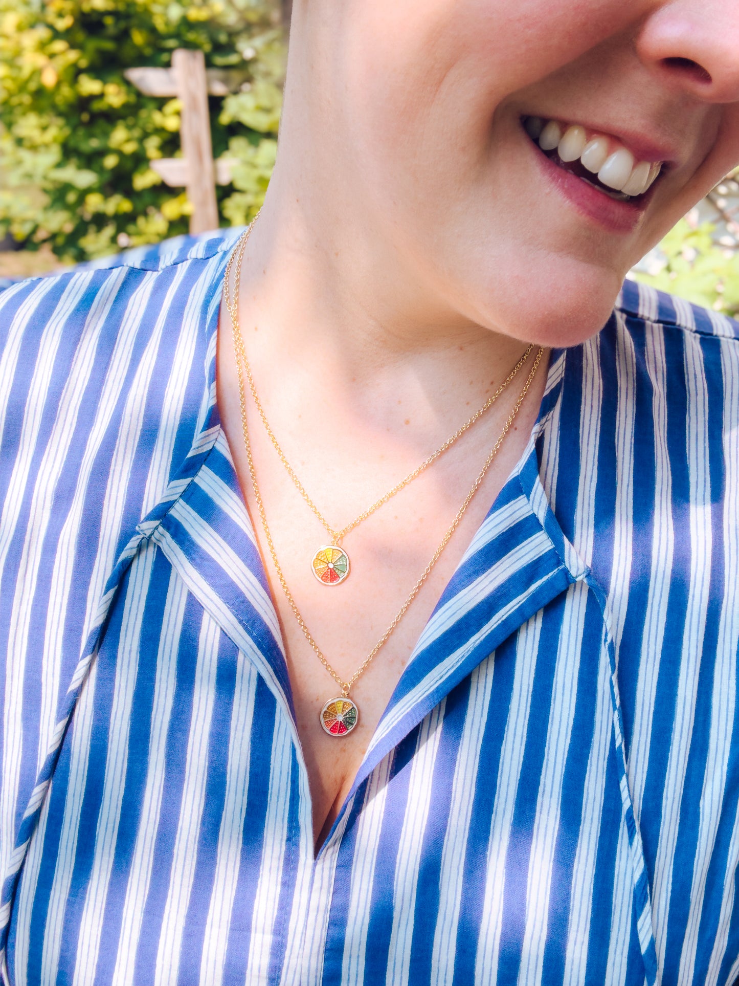 Person wearing a blue and white striped shirt with a gold necklace featuring a colorful pendant.