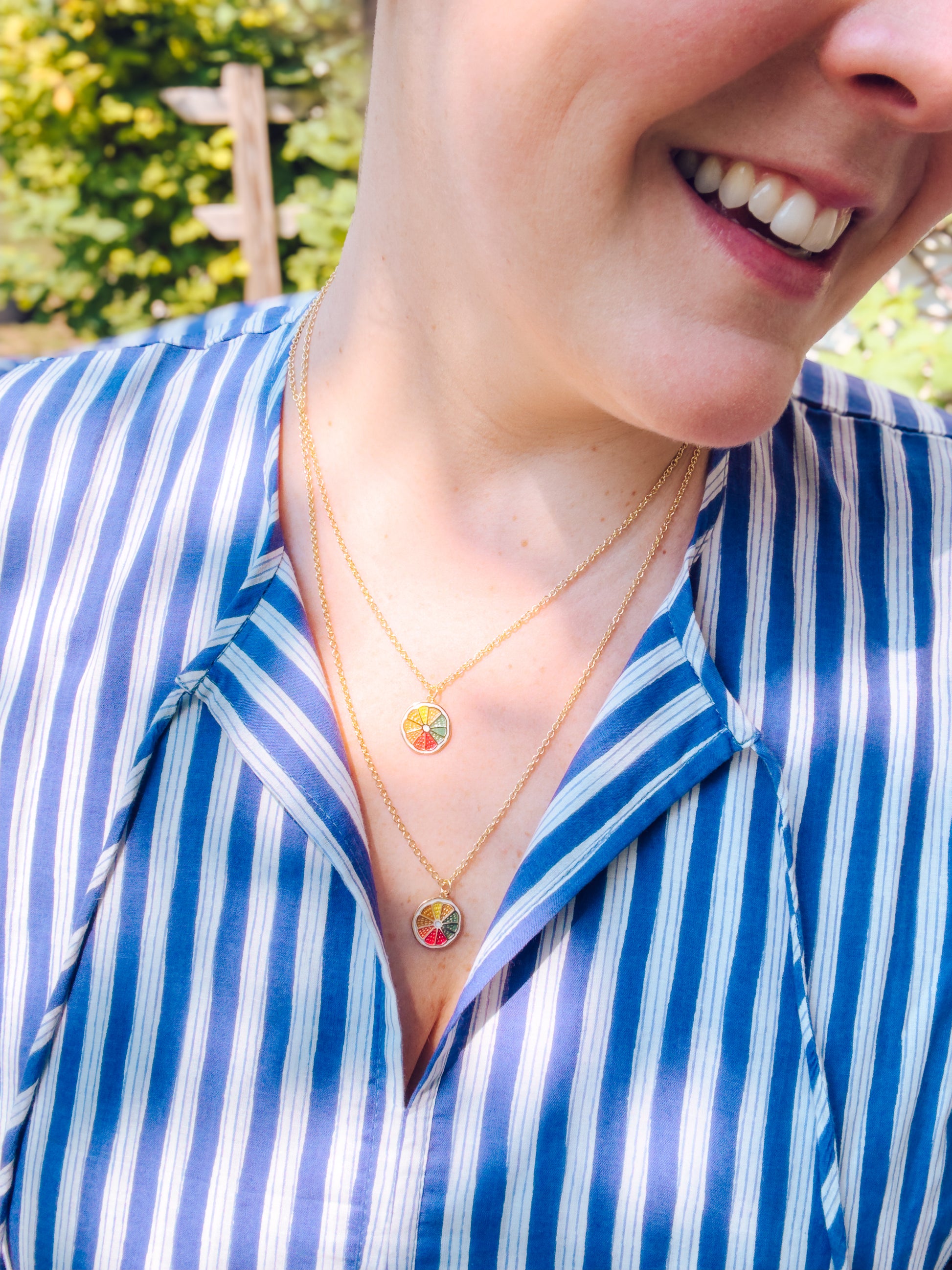 Person wearing a blue and white striped shirt with a gold necklace featuring a colorful pendant.