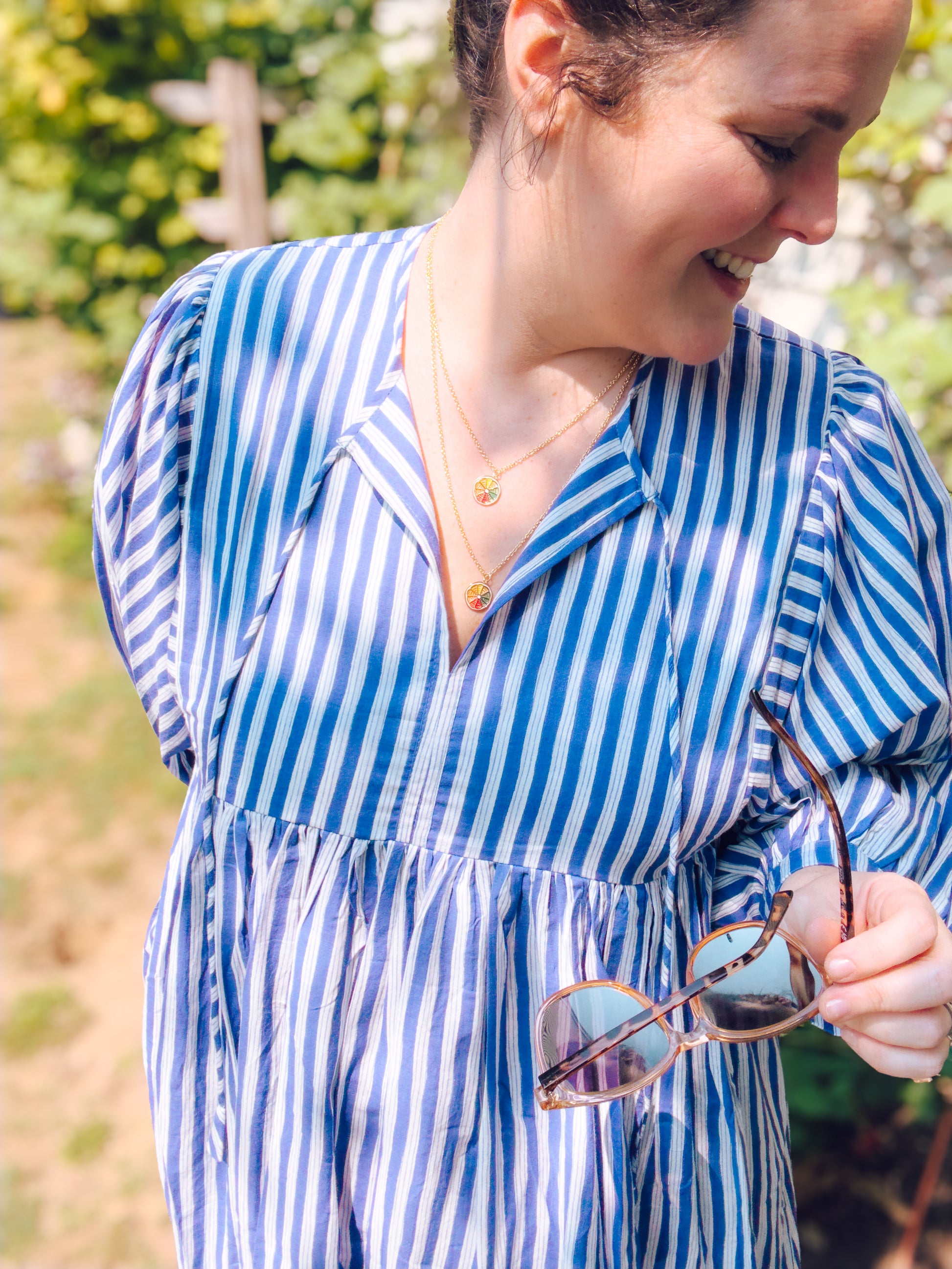 Woman in a blue and white striped dress holding sunglasses outdoors.