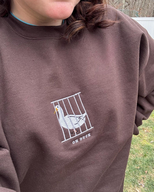 Brown sweatshirt with a white graphic of a duck in a cage and 'Oh Duck' text.
