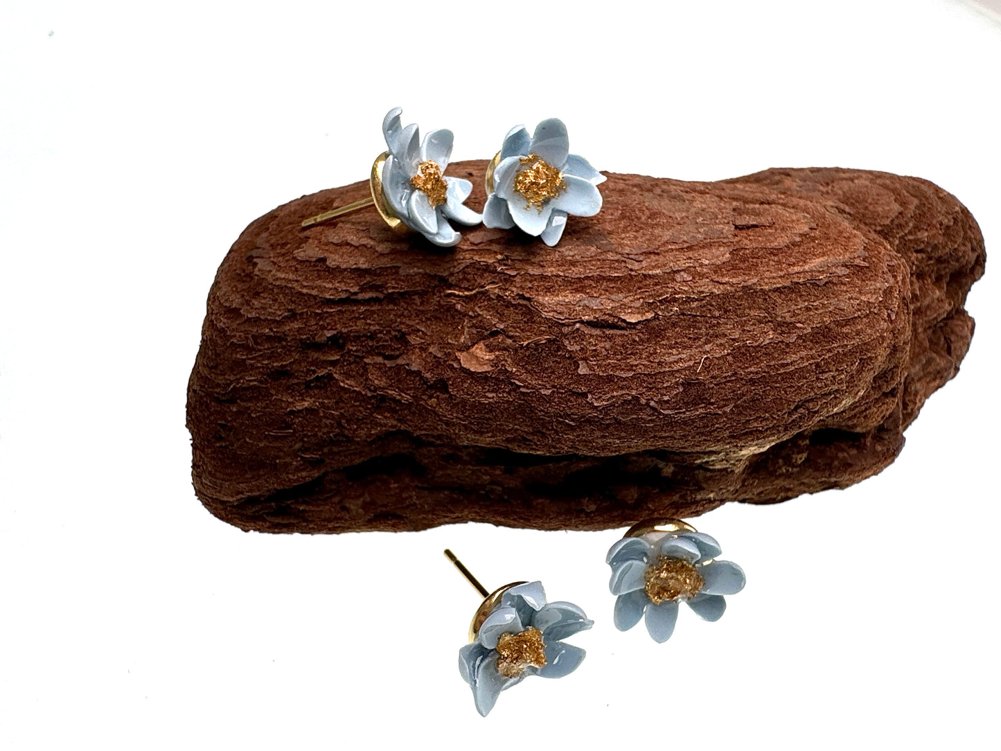 Floral earrings on a piece of brown wood with a white background