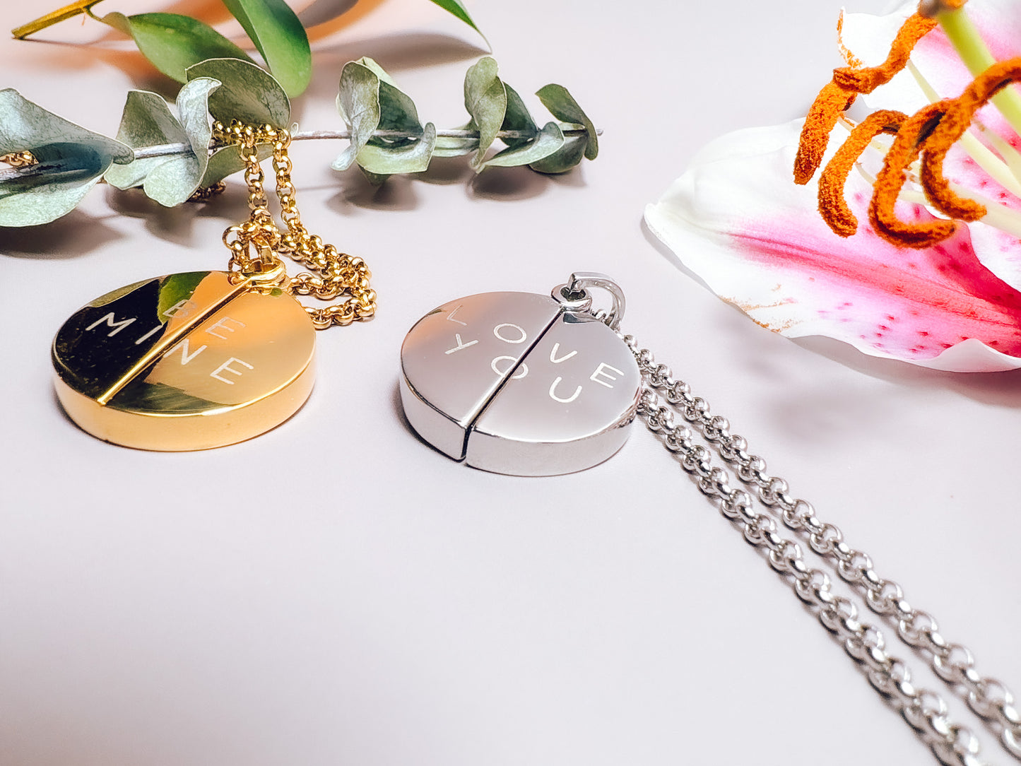 Two round pendants on chains with 'LOVE' engraved, one gold and one silver, on a light background.