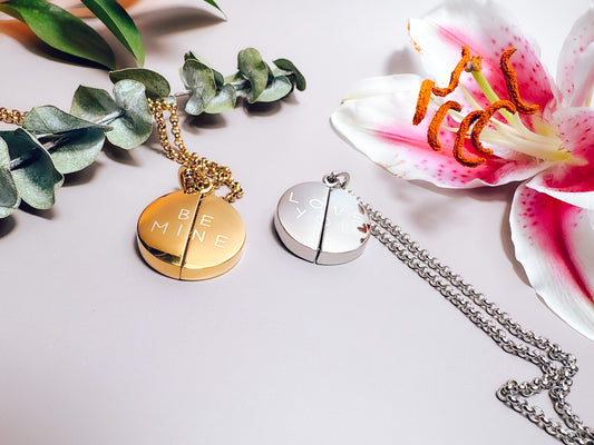 Two necklaces with round pendants on a white surface with flowers and leaves.