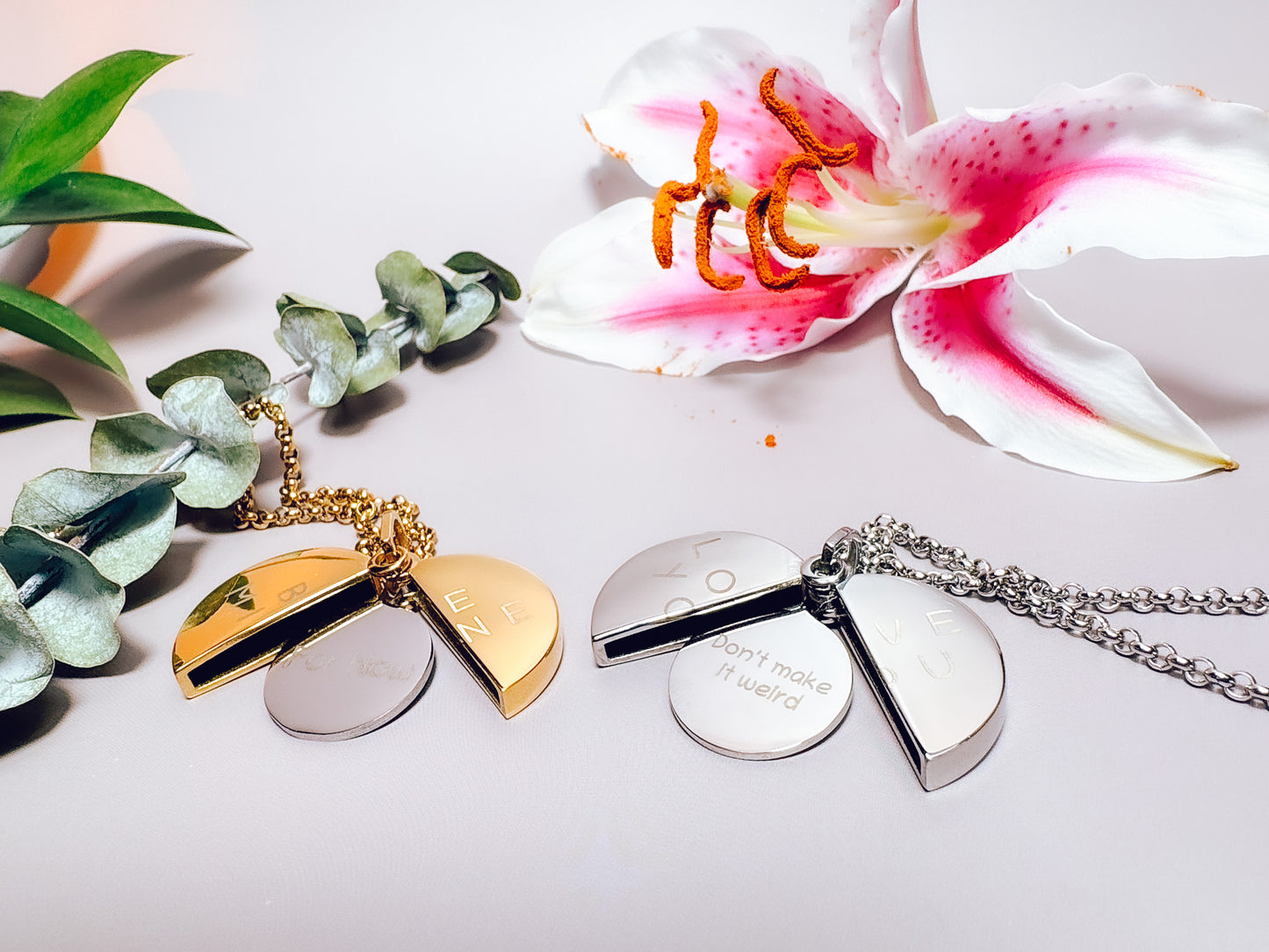 Two necklaces with pendants on a white surface with a flower and leaves in the background.