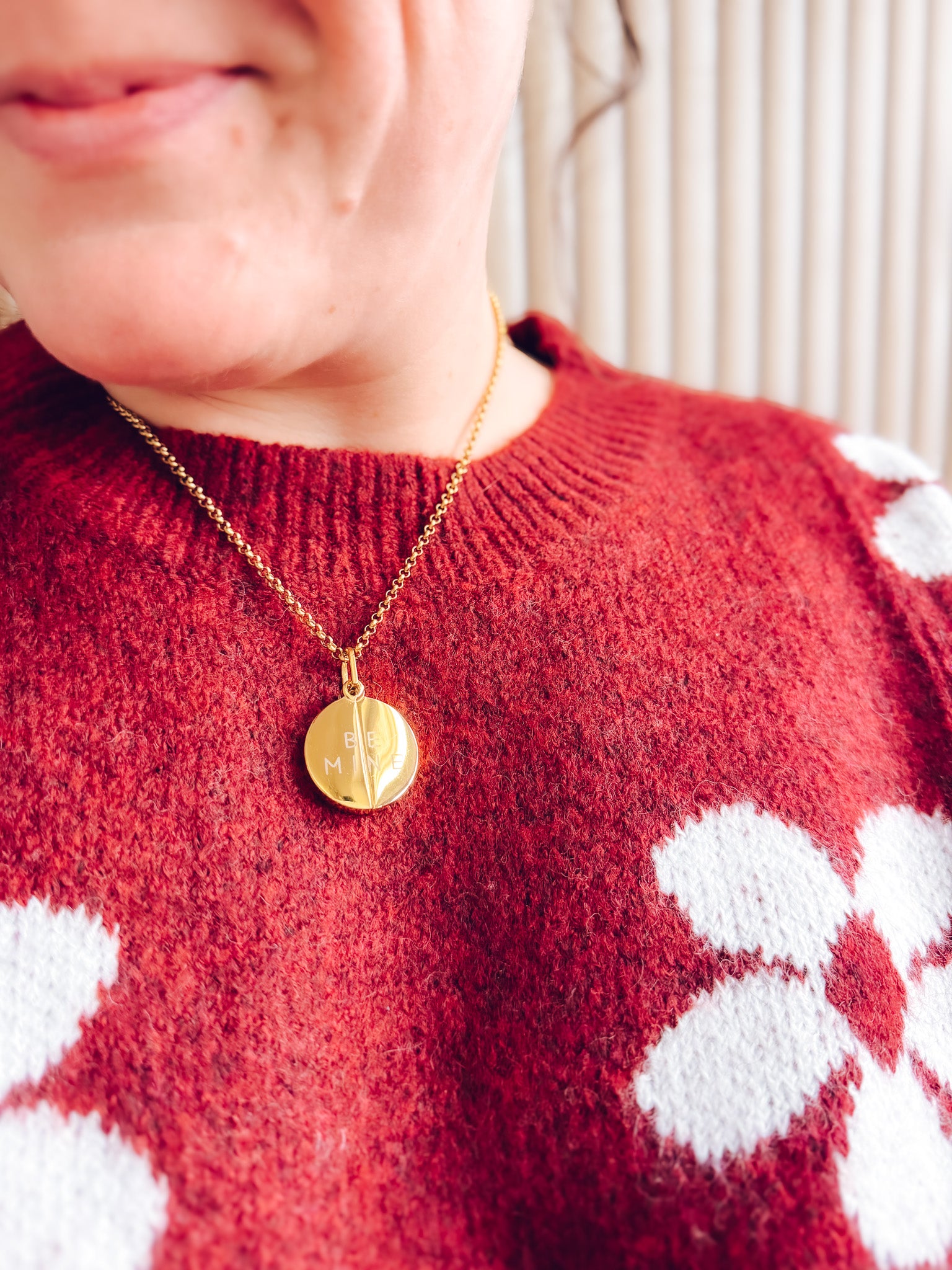 Person wearing a red sweater with white patterns and a gold necklace.