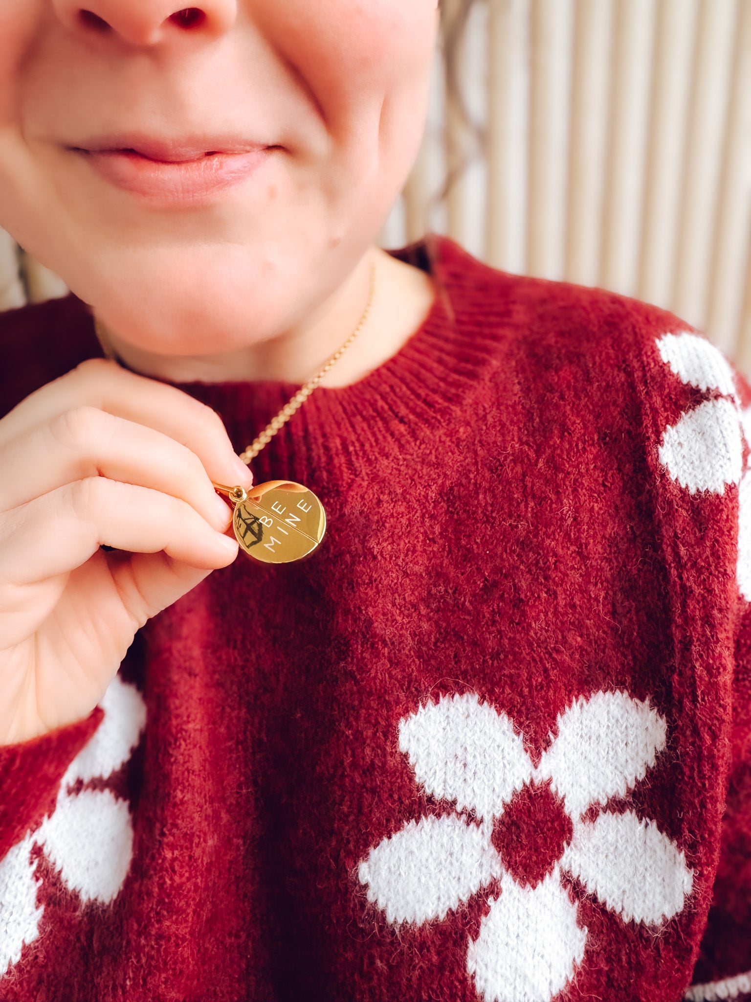 Person wearing a red sweater with white patterns, holding a gold necklace with a round pendant.