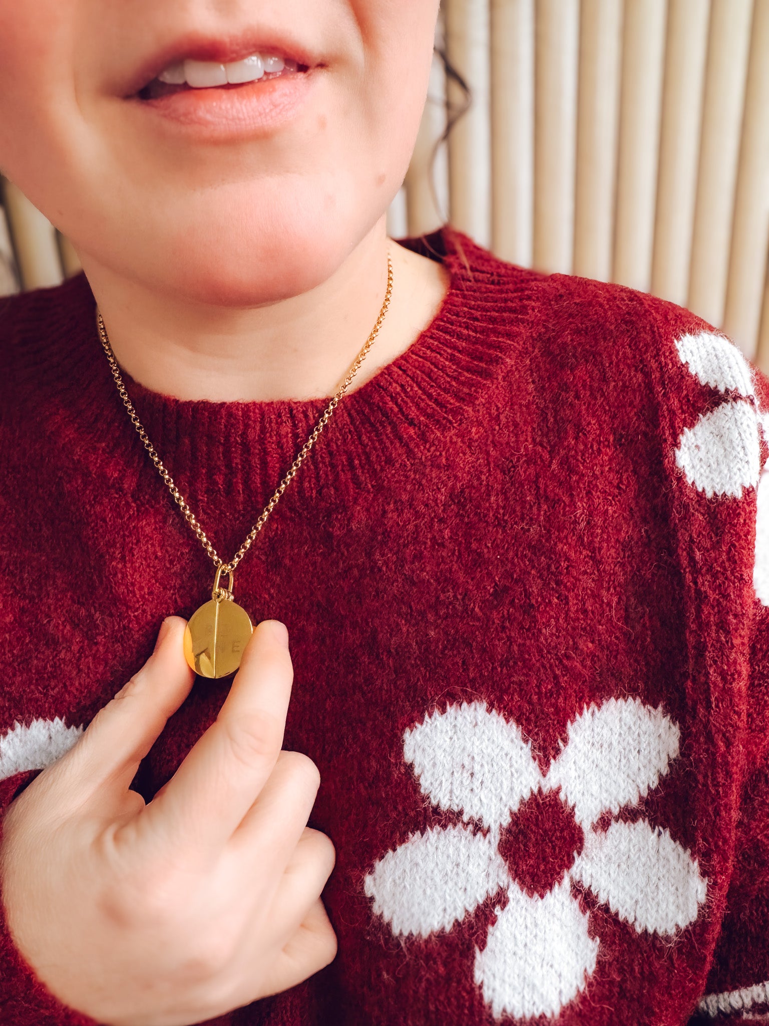 Person wearing a red sweater with white floral patterns and holding a gold necklace.
