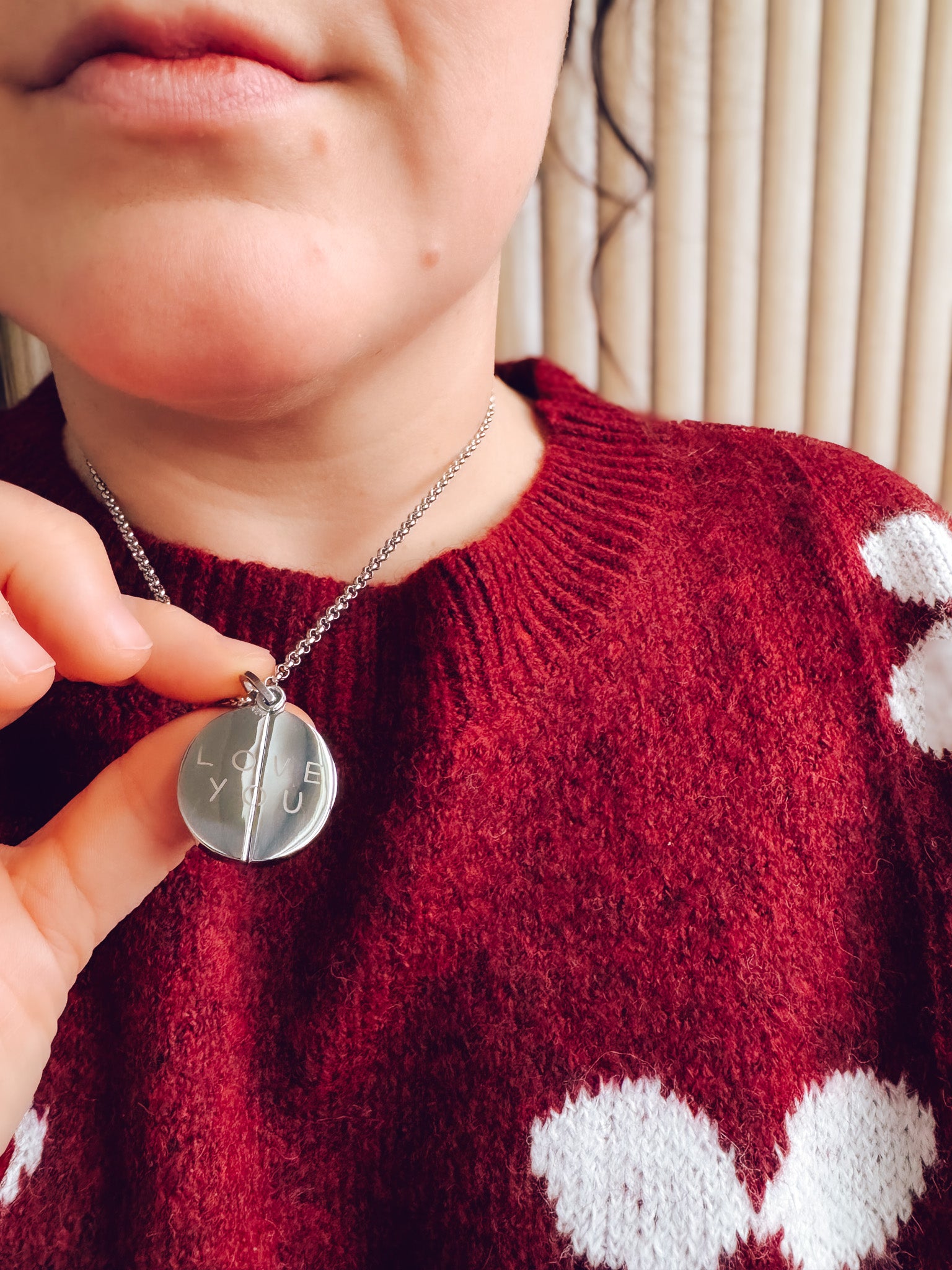 Person wearing a red sweater with white patterns, holding a necklace with a pendant.