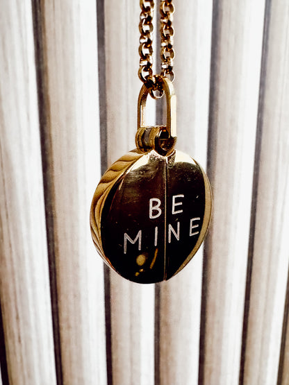 Necklace with a pendant that says 'BE MINE' against a striped background