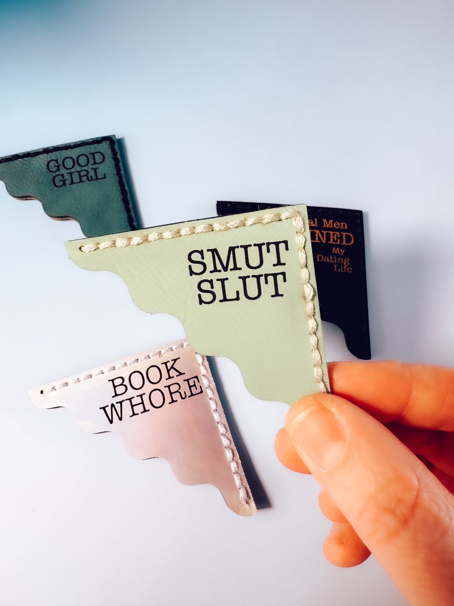 Hand holding a book with text 'Smut Slut' among other books on a light background