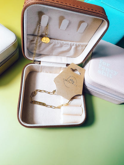 Open jewelry case with gold necklaces and a visible brand tag on a green surface.