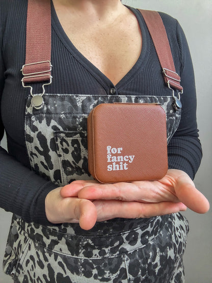 Person holding a brown leather case with text, wearing a black shirt and patterned apron.
