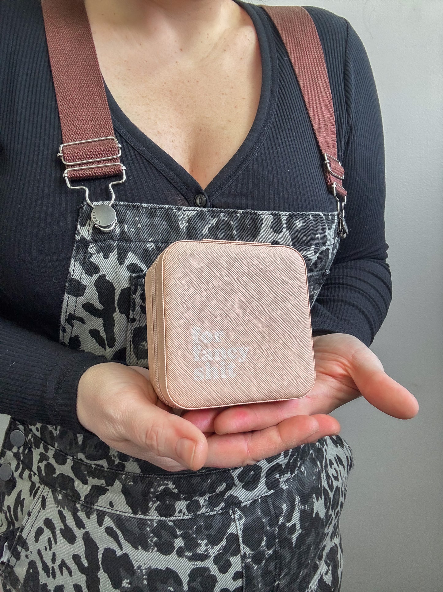 Person holding a pink compact mirror with text, wearing a patterned apron.