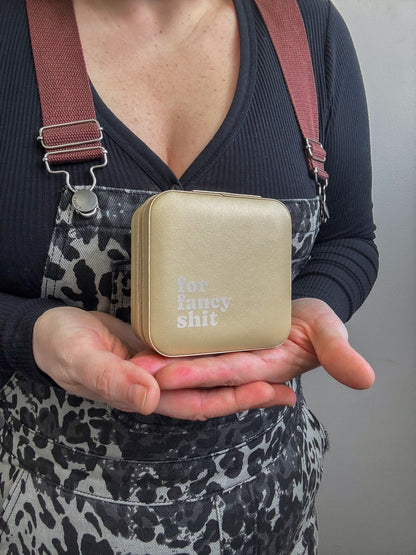 Person holding a beige square pouch with text, wearing a dark top and patterned apron.