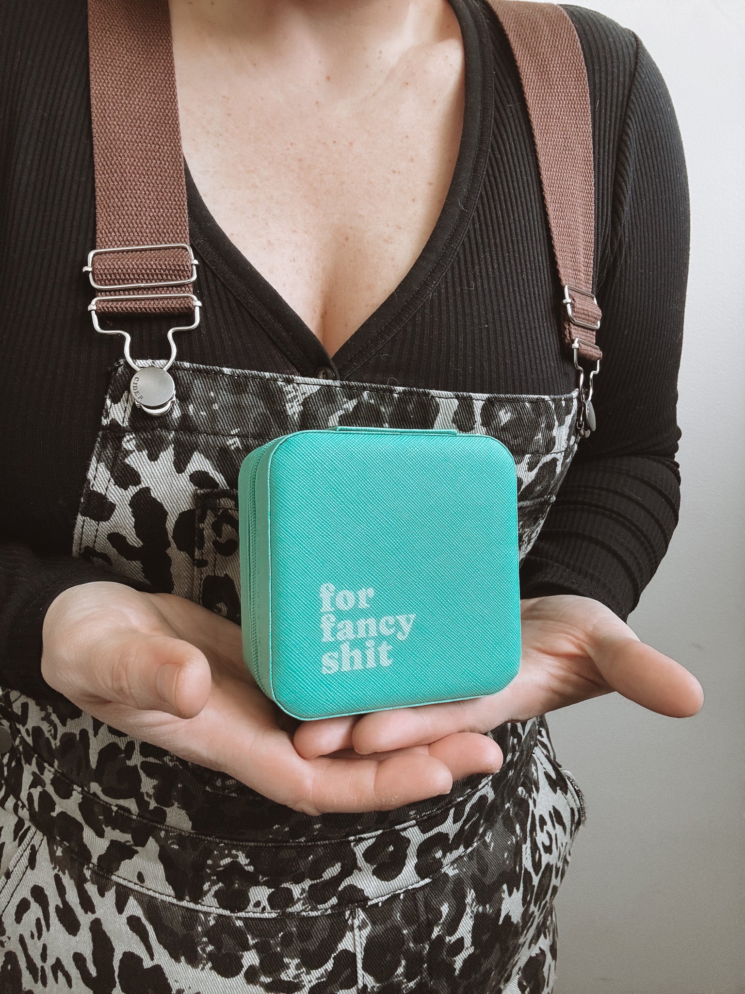 Person holding a turquoise box with text, wearing a black top and leopard print apron.