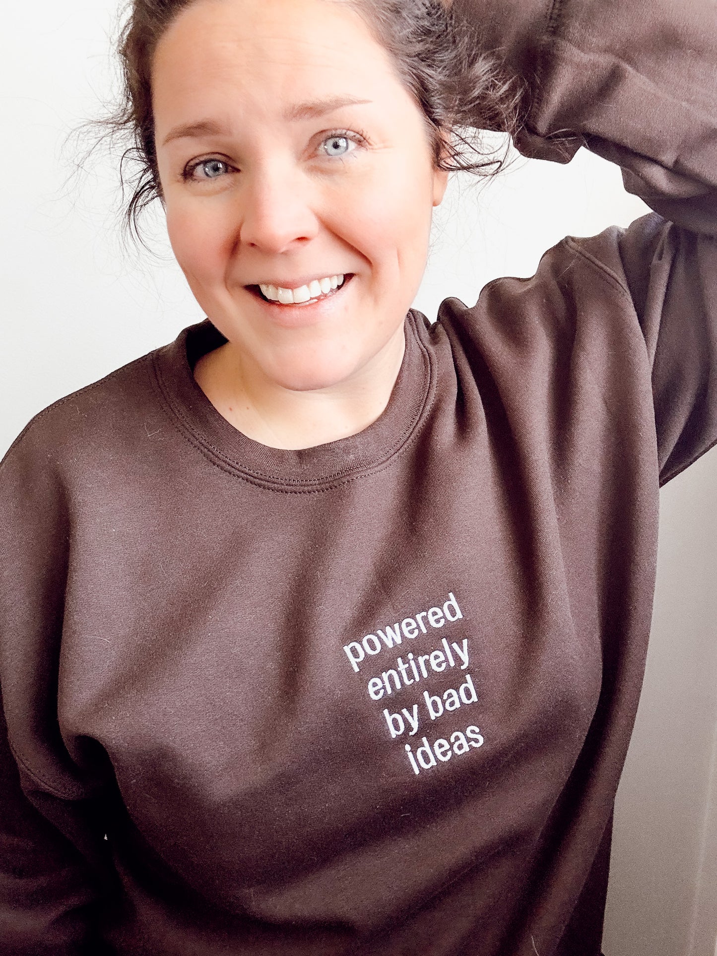 Person wearing a brown sweatshirt with text, smiling against a white background